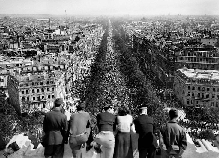 Imágenes Históricas Personal del Ejército de los EE. UU. de pie en la cima del Arco del Triunfo en París mirando la festiva marcha masiva que marca el final de la Segunda Guerra Mundial