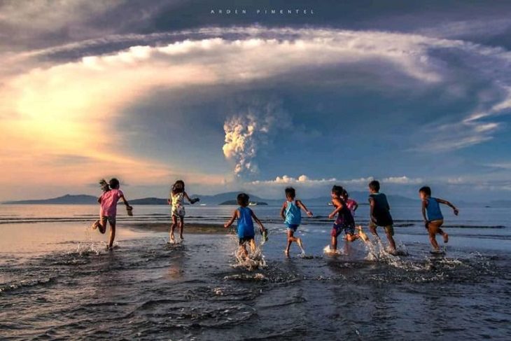 Erupción Del Volcán Taal En Filipinas niños corriendo con la playa con fondo de la explosión del volcán