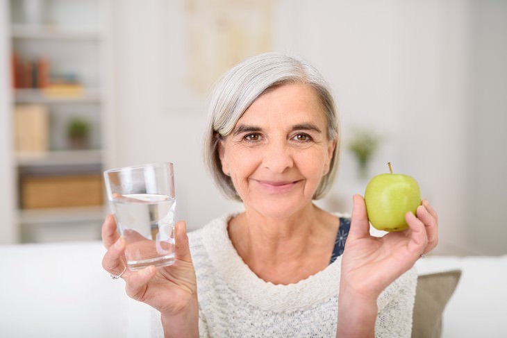 deshidratación en personas mayores anciana sosteniendo un vaso de agua en una mano y una manzana en la otra
