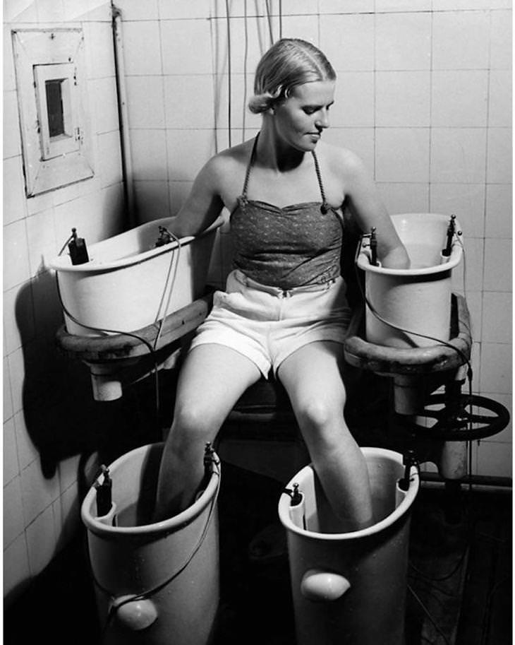 Prácticas De Belleza Del Pasado Una mujer joven sostiene sus brazos y piernas en cuatro baños de agua con corriente eléctrica para mejorar la circulación sanguínea, c. 1938