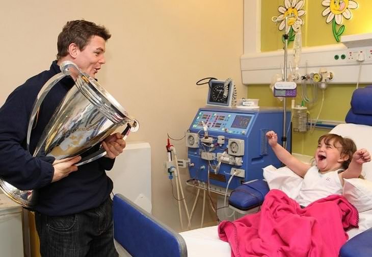 El jugador irlandés de rugby, Brian O'Driscoll, visitando y mostrándole el trofeo a una niña en el hospital