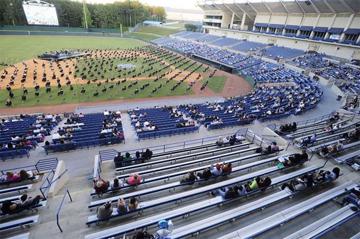Estudiantes de bachillerato sentados en un campo de béisbol durante su distanciada ceremonia de graduación