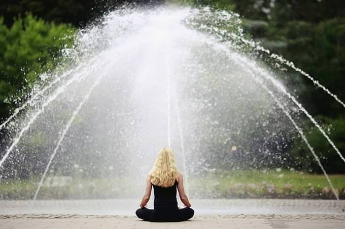 Una mujer meditando frente a una fuente.