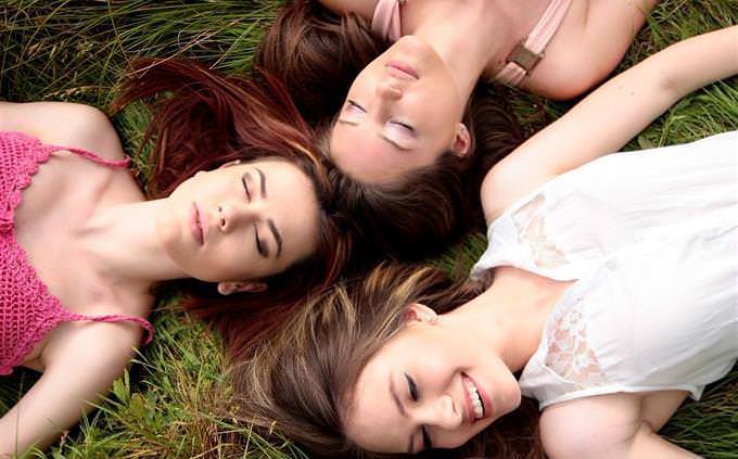three girls lying in the grass heads together