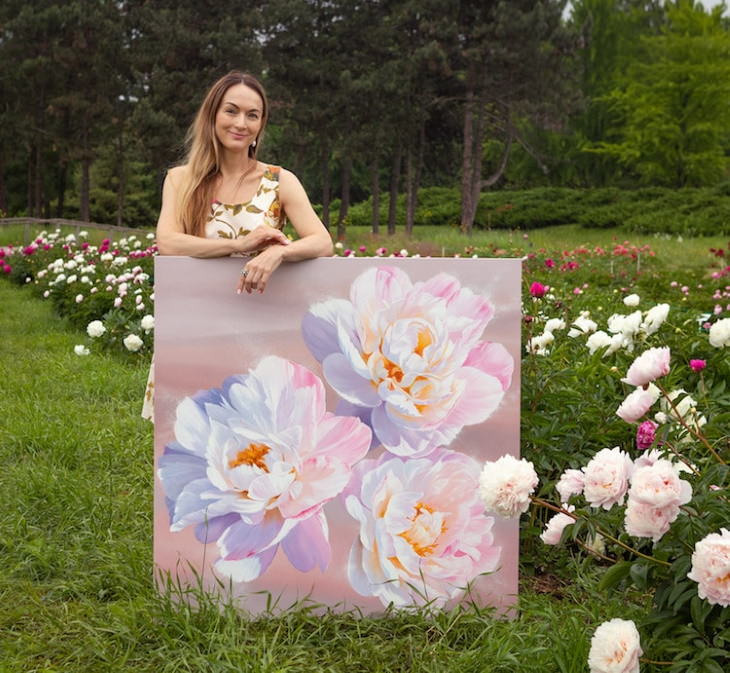 Pinturas Florales De Ira Volkova la artista posando con su pintura en un jardín