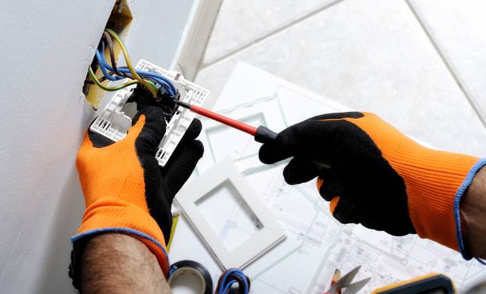 Mitos de la electricidad, las manos con guantes de seguridad fijando la toma de corriente
