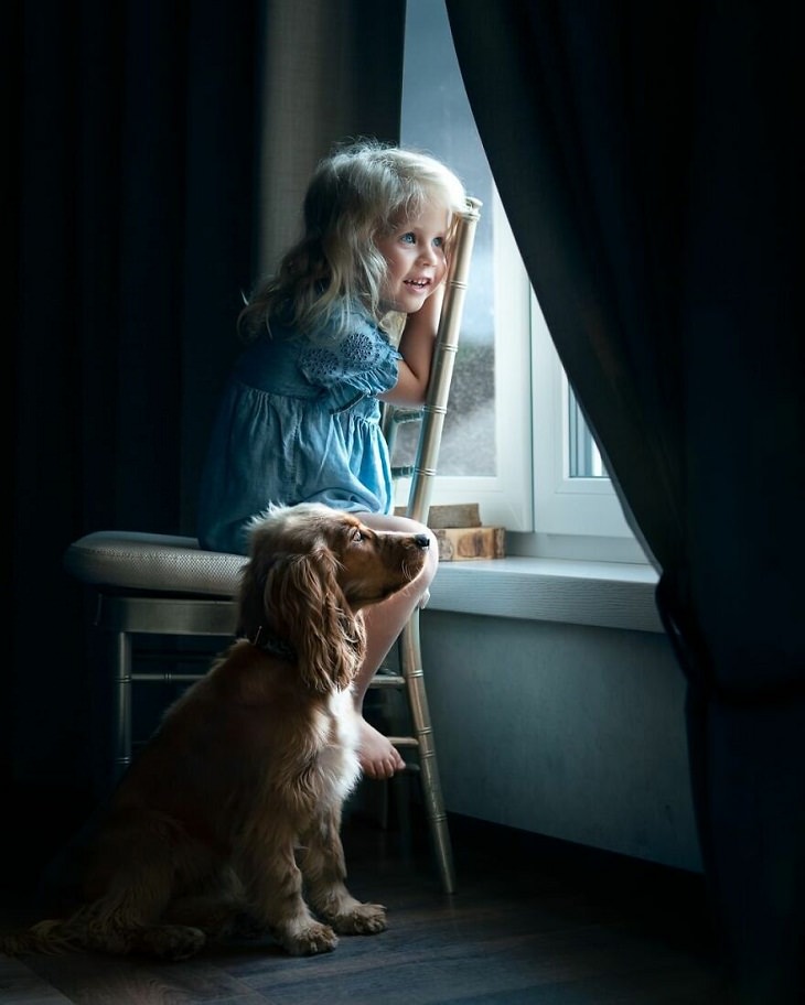Fotos Mágicas Que Capturan El Encanto De La Infancia, Niña y su perro miran por la ventana