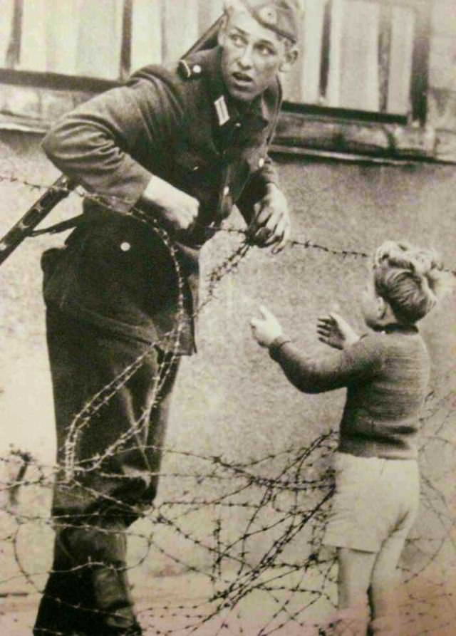 Fotos Eventos Históricos, Un soldado alemán que va en contra de las órdenes directas de ayudar a un niño a cruzar el Muro de Berlín