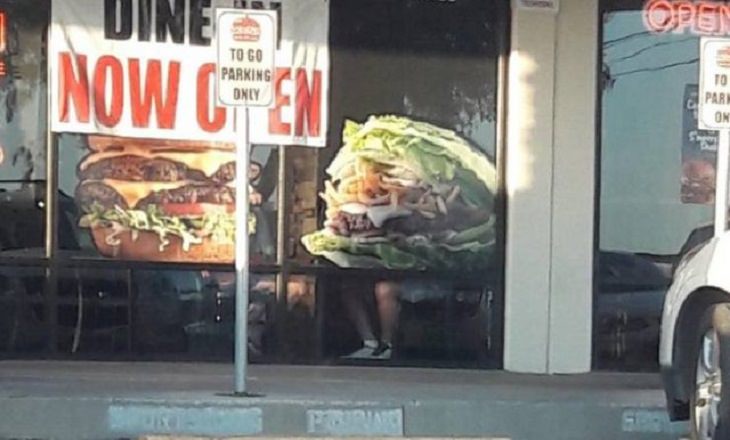 Fotografías que te harán mirar dos veces o hacer una doble toma, Foto grande de hamburguesa con las piernas visibles de una persona sentada frente a ella