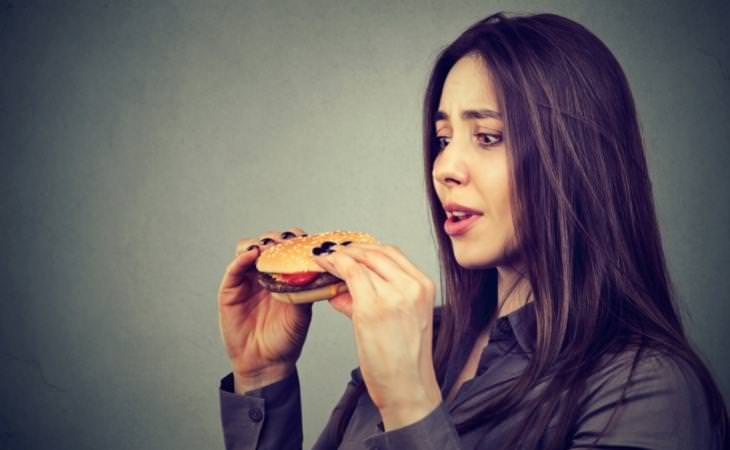 תחושת השתוקקות למאכלים: אישה אוחזת המבורגר ומתבוננת בו