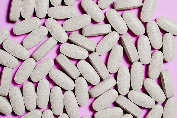 Píldoras de suplementos innecesarios sobre un fondo rosa