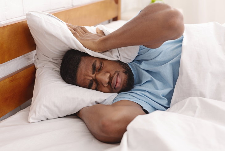 Síndrome de la cabeza explosiva hombre tratando de dormir en una habitación ruidosa