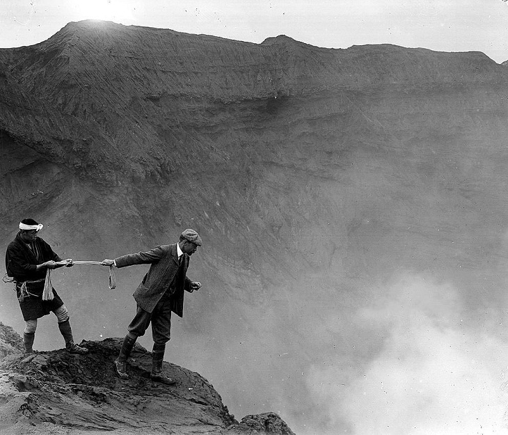 Un hombre inclinado sobre el borde para mirar hacia el interior del cráter del Monte Aso, también conocido como Volcán Aso, Japón (c. 1906)