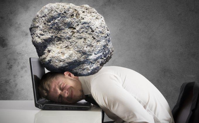 Estás agotado o estresado: hombre con una piedra presionando su cabeza directamente en una computadora portátil