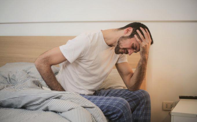 Estás agotado o estresado: un hombre se sienta en una cama sosteniendo su cabeza
