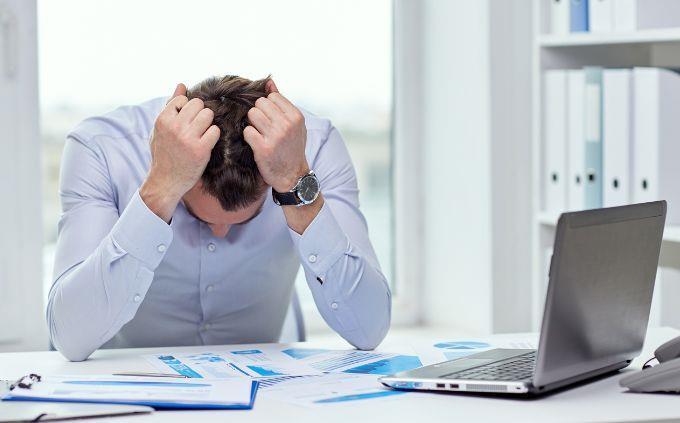 Estás agotado o estresado: un hombre frente a una computadora sosteniendo su cabeza