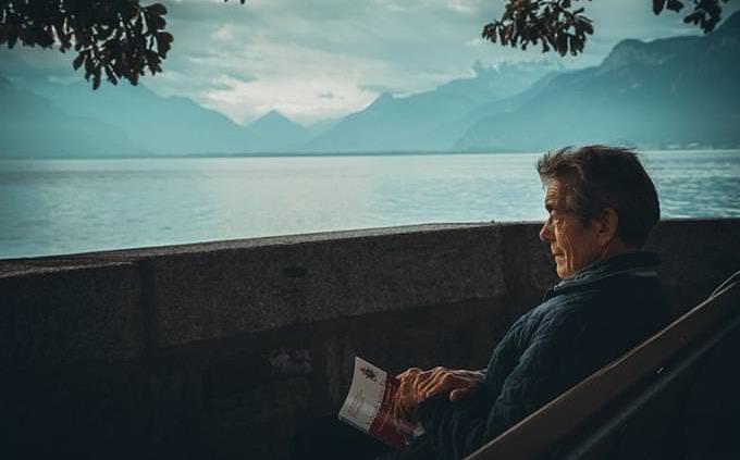 Un anciano sentado al borde de un lago con un libro