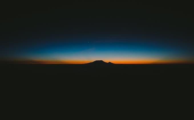 Luz naranja contra el cielo y una sombra de montañas.